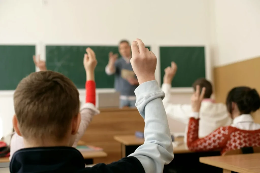 classe scolastica di bambini che alzano la mano perchè conoscono la risposta